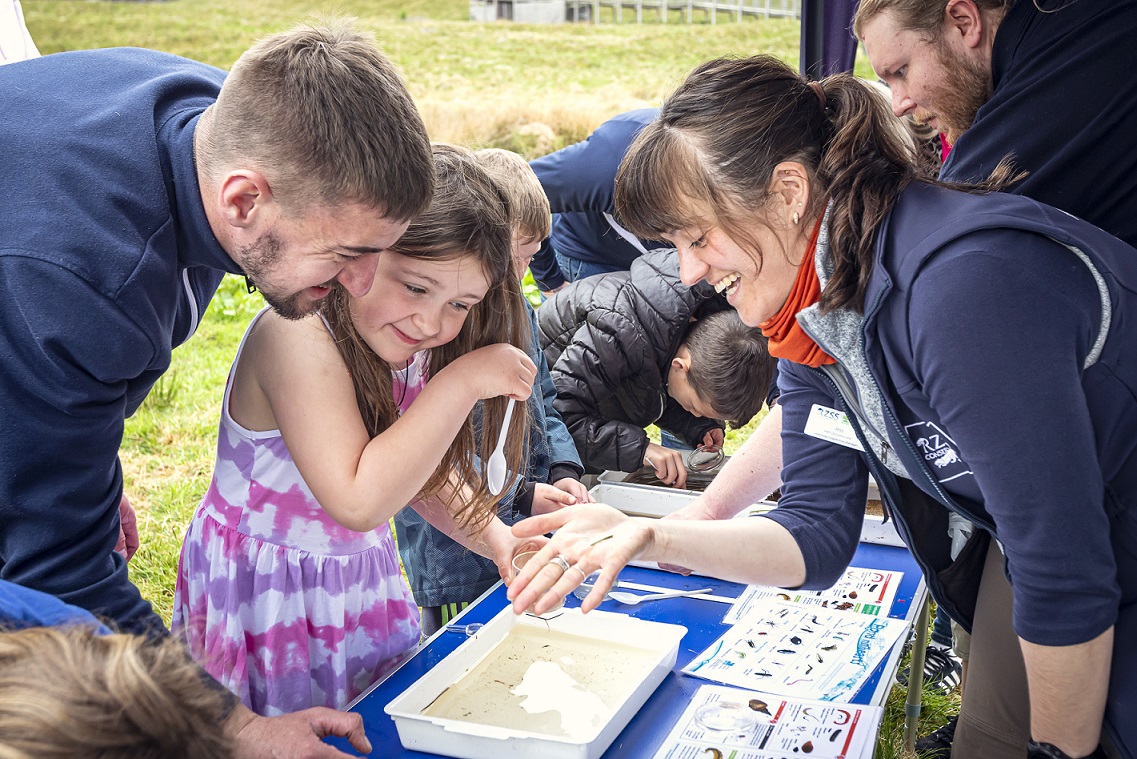 HWP pond dipping session. Child (a girl) is looking at a tray while parent and HWP team member Jess Wise looks over them IMAGE: Unknown 2024